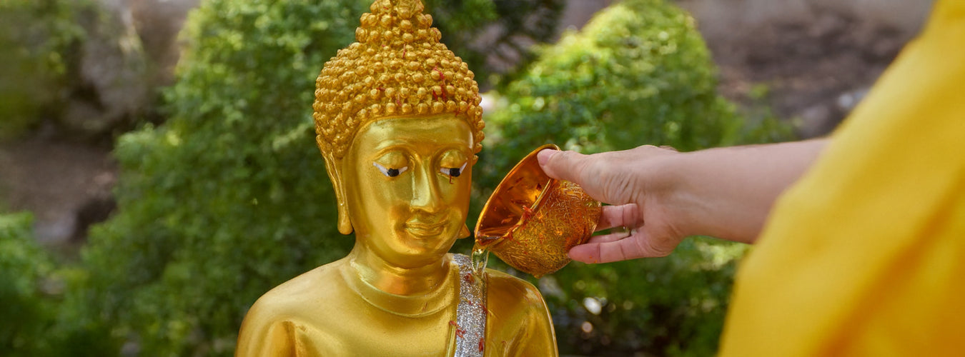 Junge Frau übergießt eine Buddha-Statue achtsam mit Wasser.
