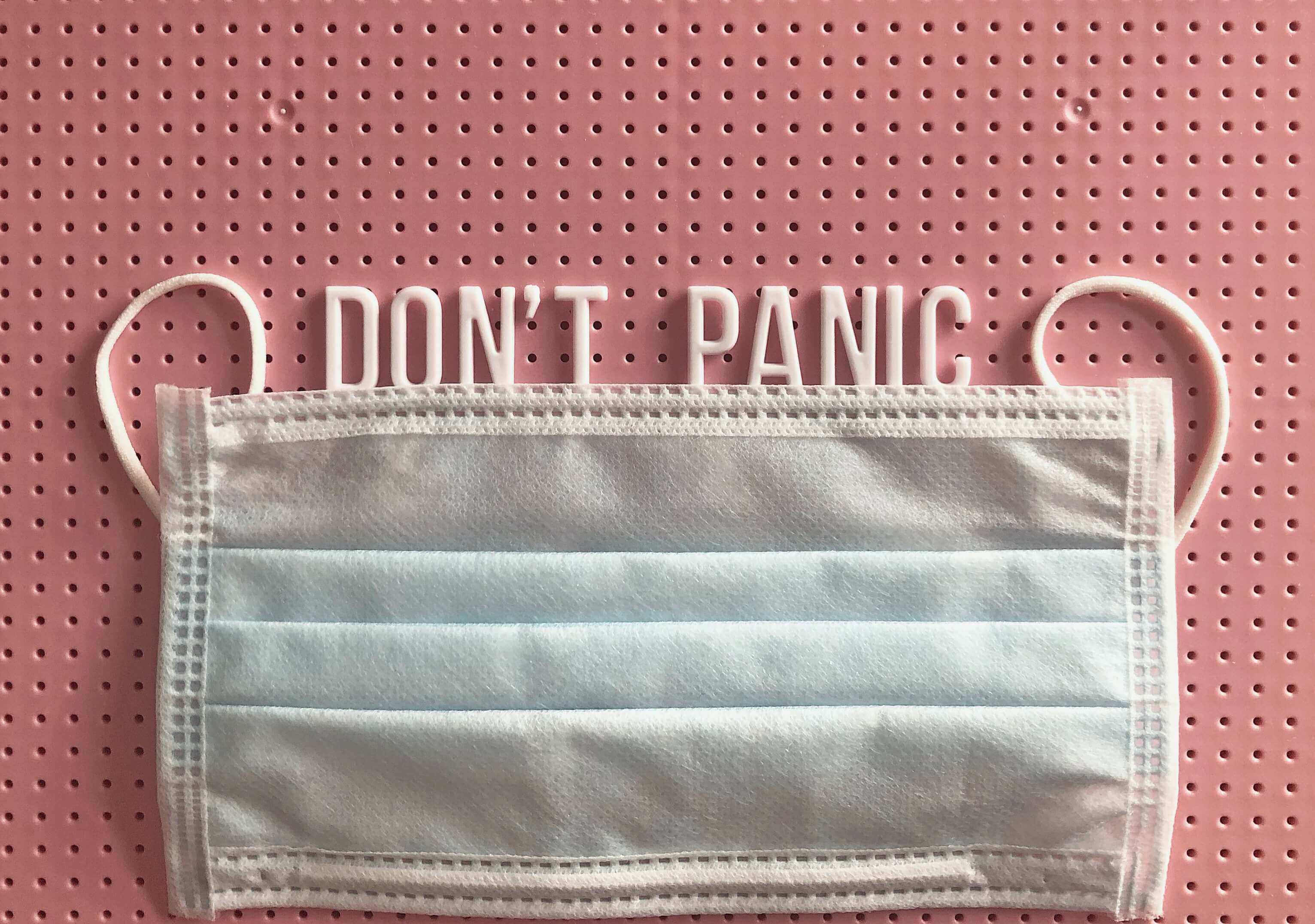 Corona Krise Angst: Mundschutz und Schrift "Don't Panic"