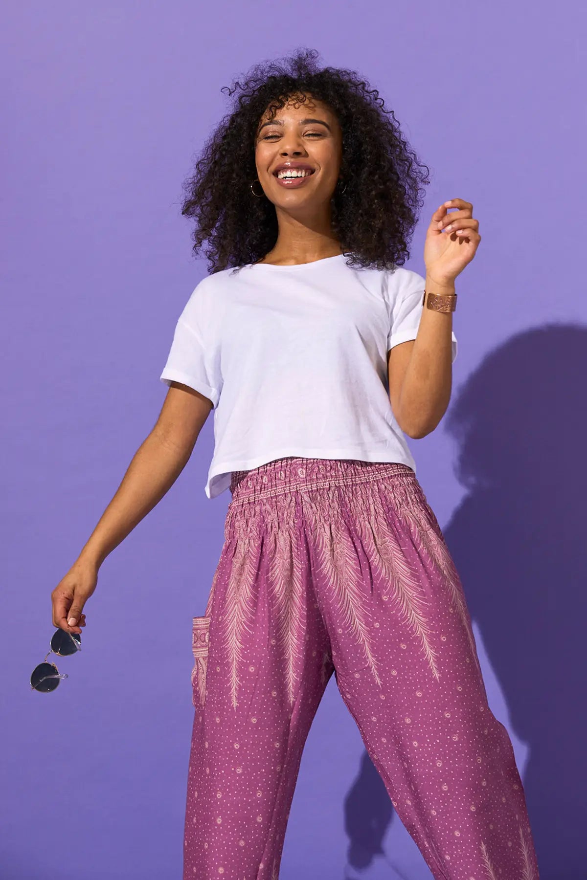 Lachende Frau in der gemusterten Haremshose in der Farbe Lila, kombiniert mit weißem Oberteil