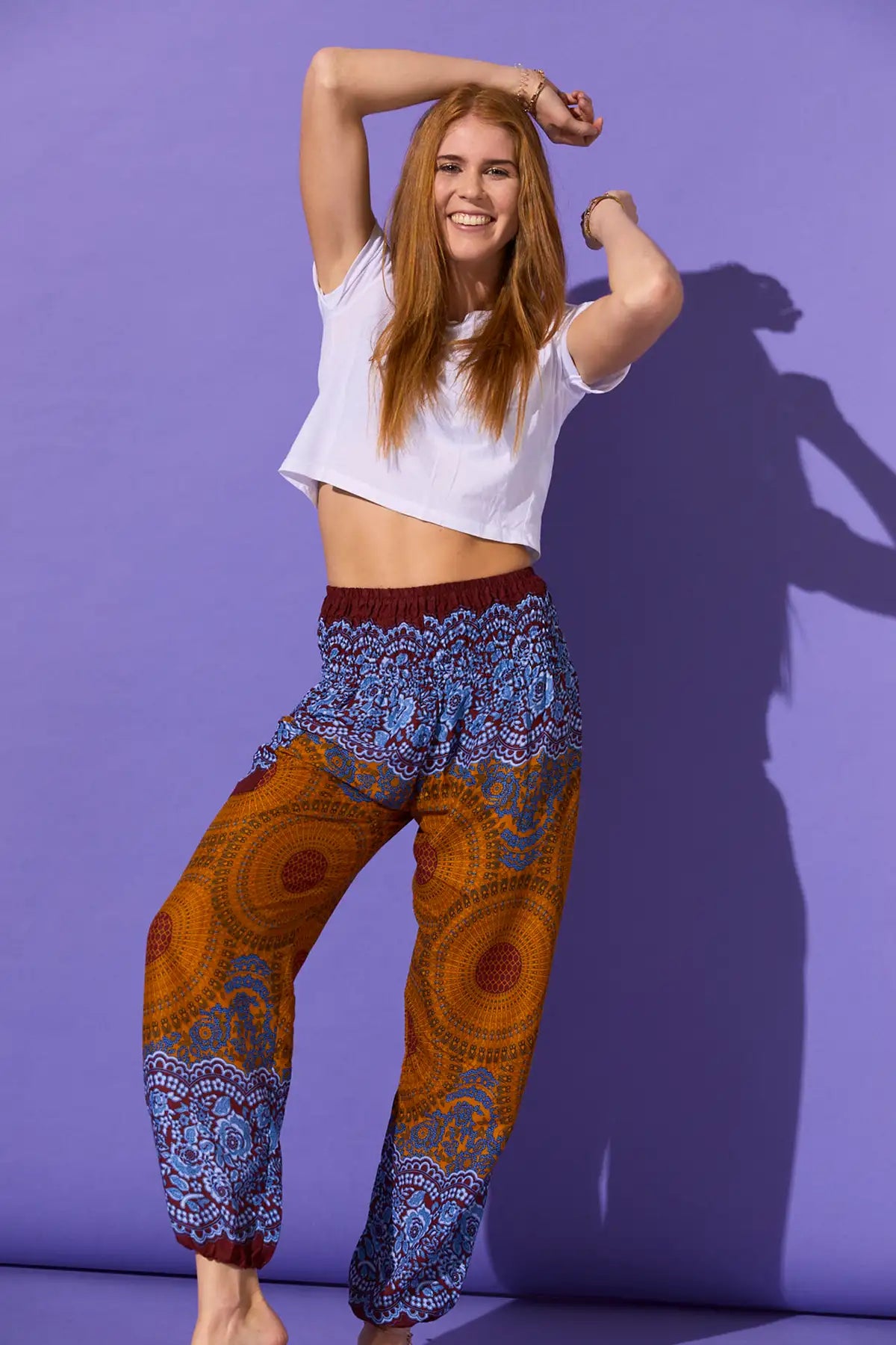 Lachende Frau in der gemusterten Haremshose in den Farben Orange und Blau, kombiniert mit weißem Oberteil