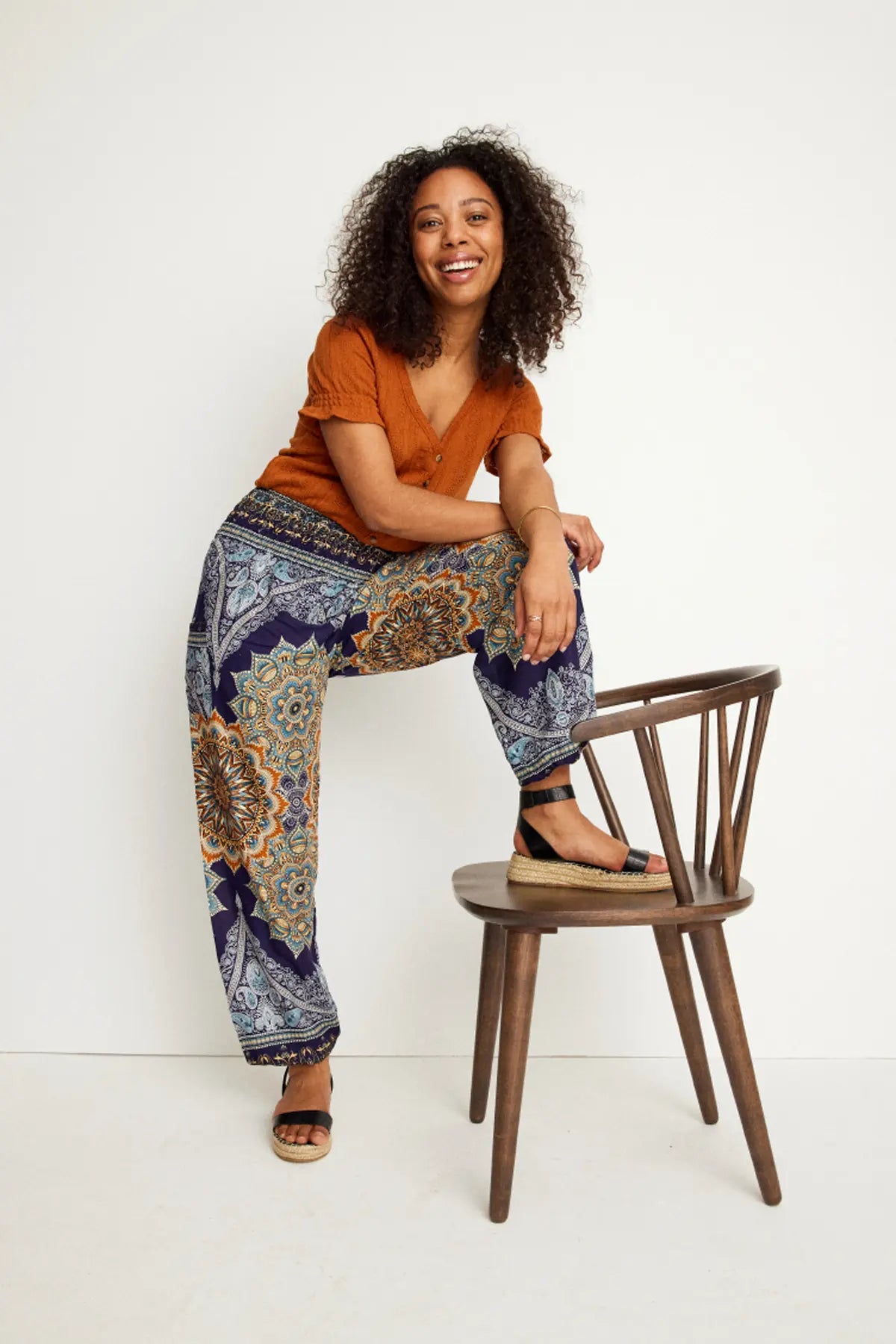 Lachende Frau in der gemusterten Haremshose in den Farben Blau und Gelb, kombiniert mit orangenem Oberteil