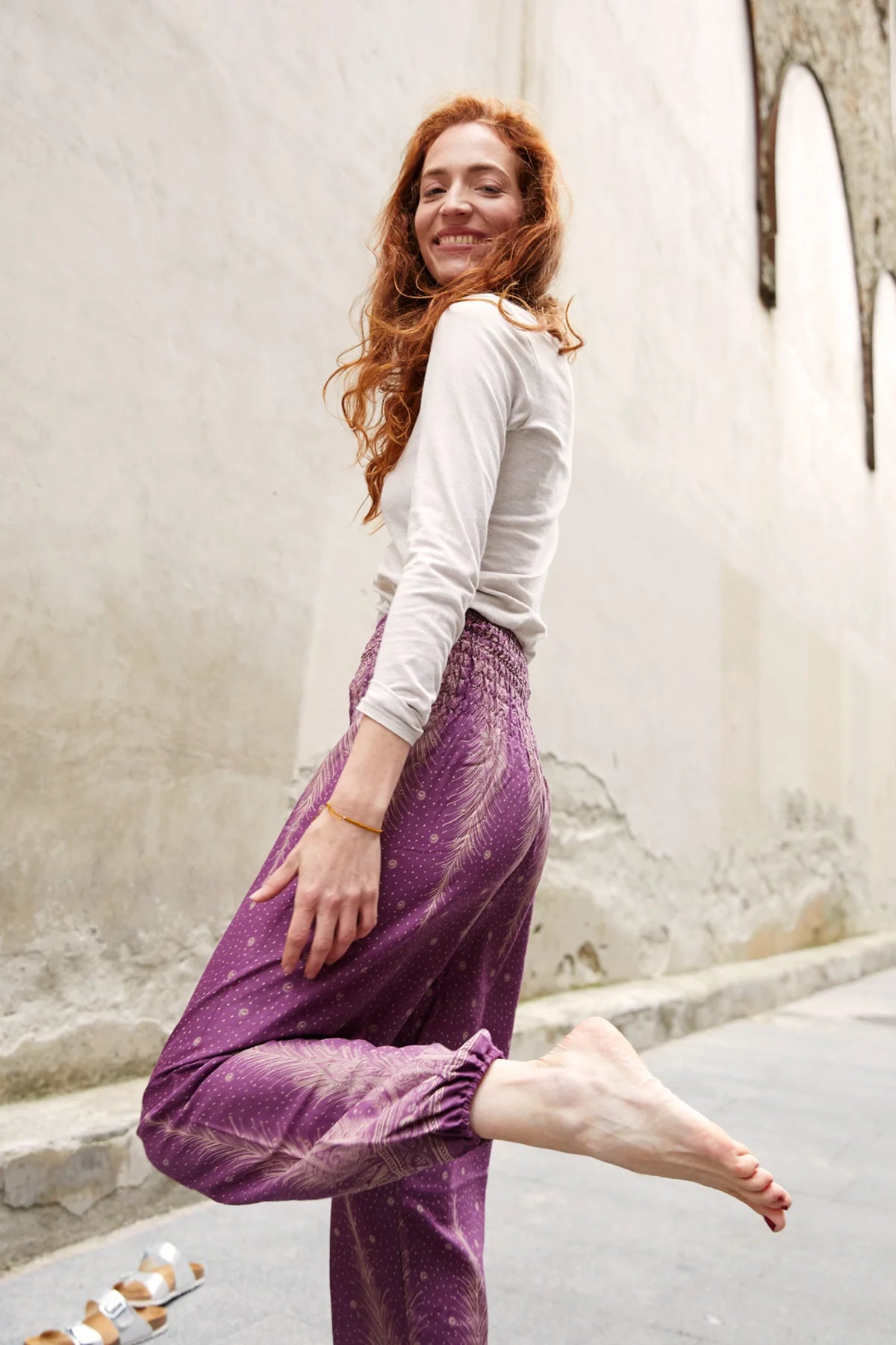 Lachende Frau in der gemusterten Haremshose in der Farbe Lila, kombiniert mit weißem Oberteil