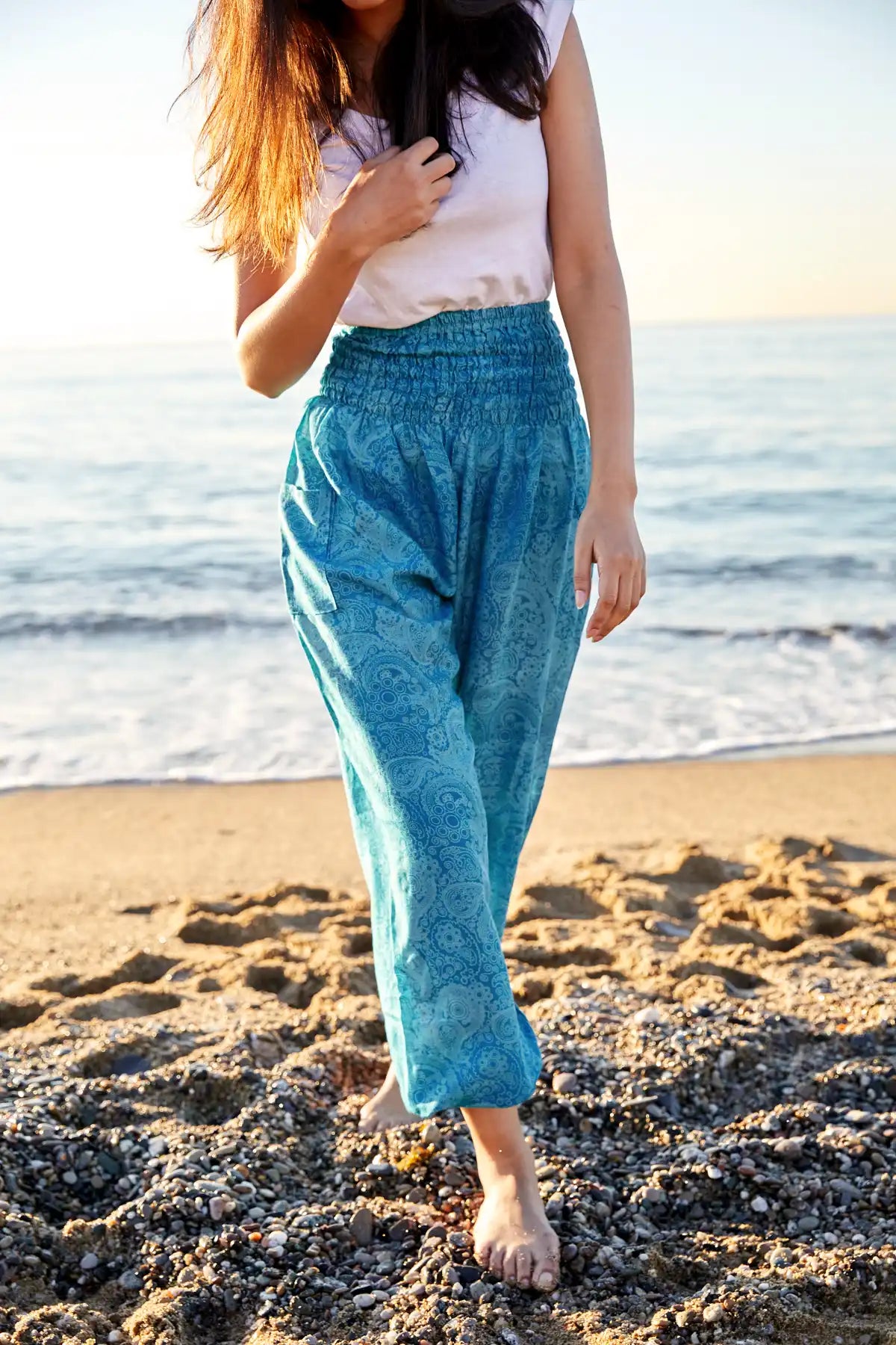 Frau am Strand in blauer gemusterten Haremshose kombiniert mit weißem Oberteil