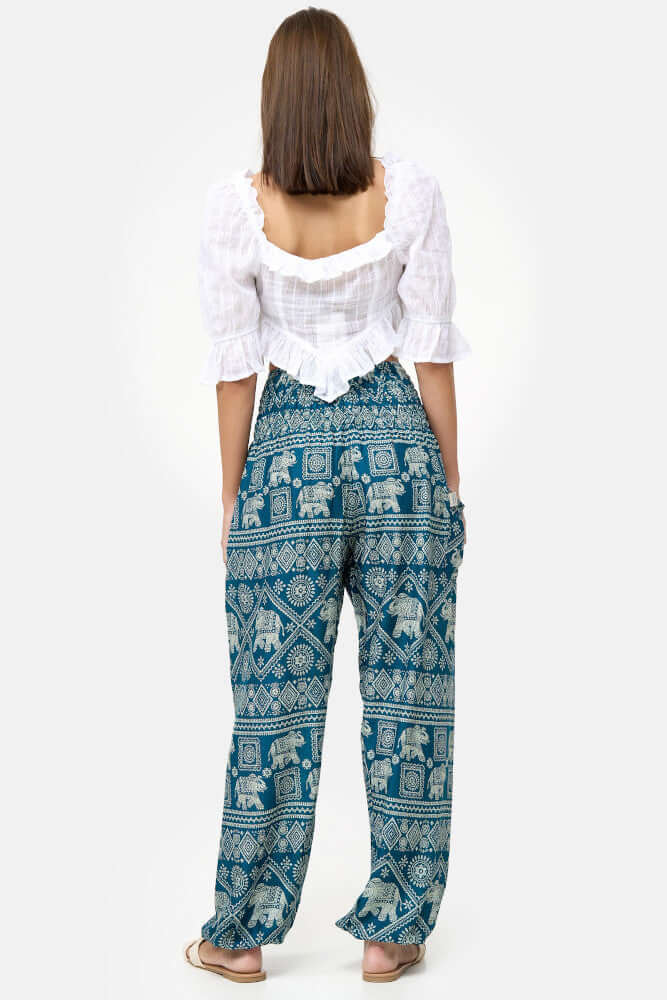 Rückansicht der stehende Frau, die die türkise Haremshose mit einem weißen Top kombiniert