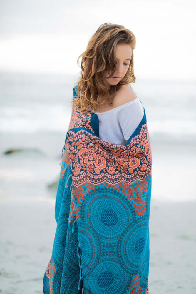 Frau am Strand wickelt sich in ein blau-orange gemustertes Tuch