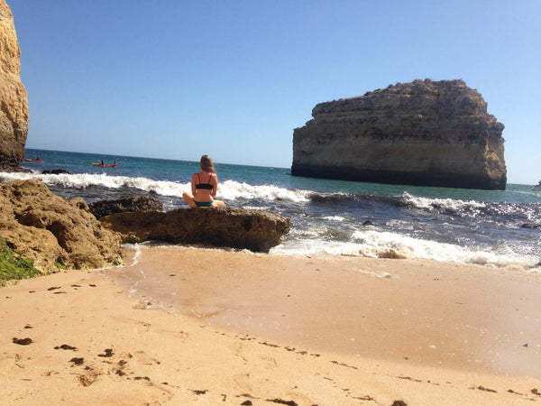 Frau sitzt im Schneidersitz am Strand auf einem Felsen