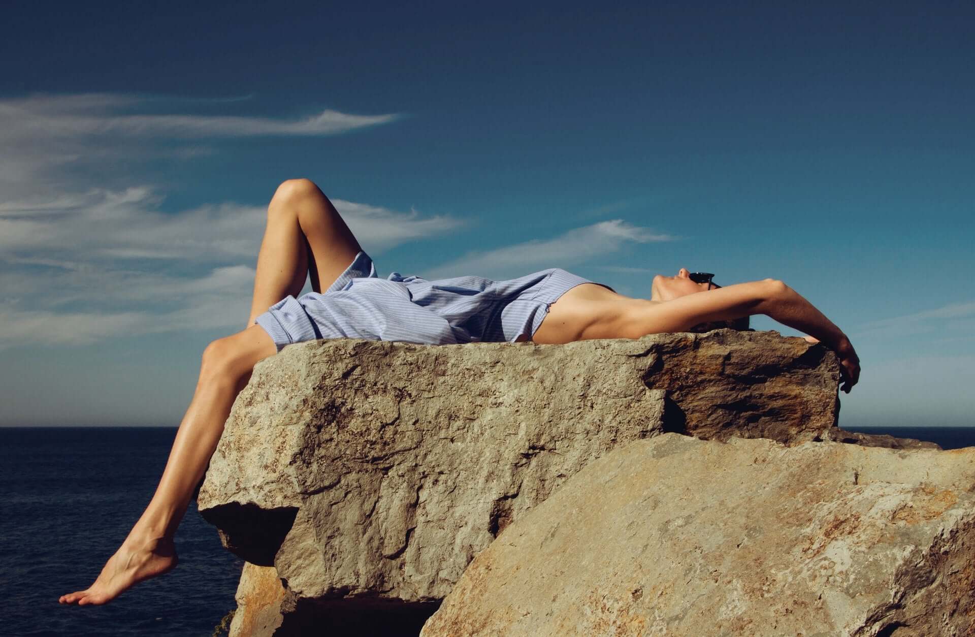 Person liegt entspannt auf einem Felsen am Meer