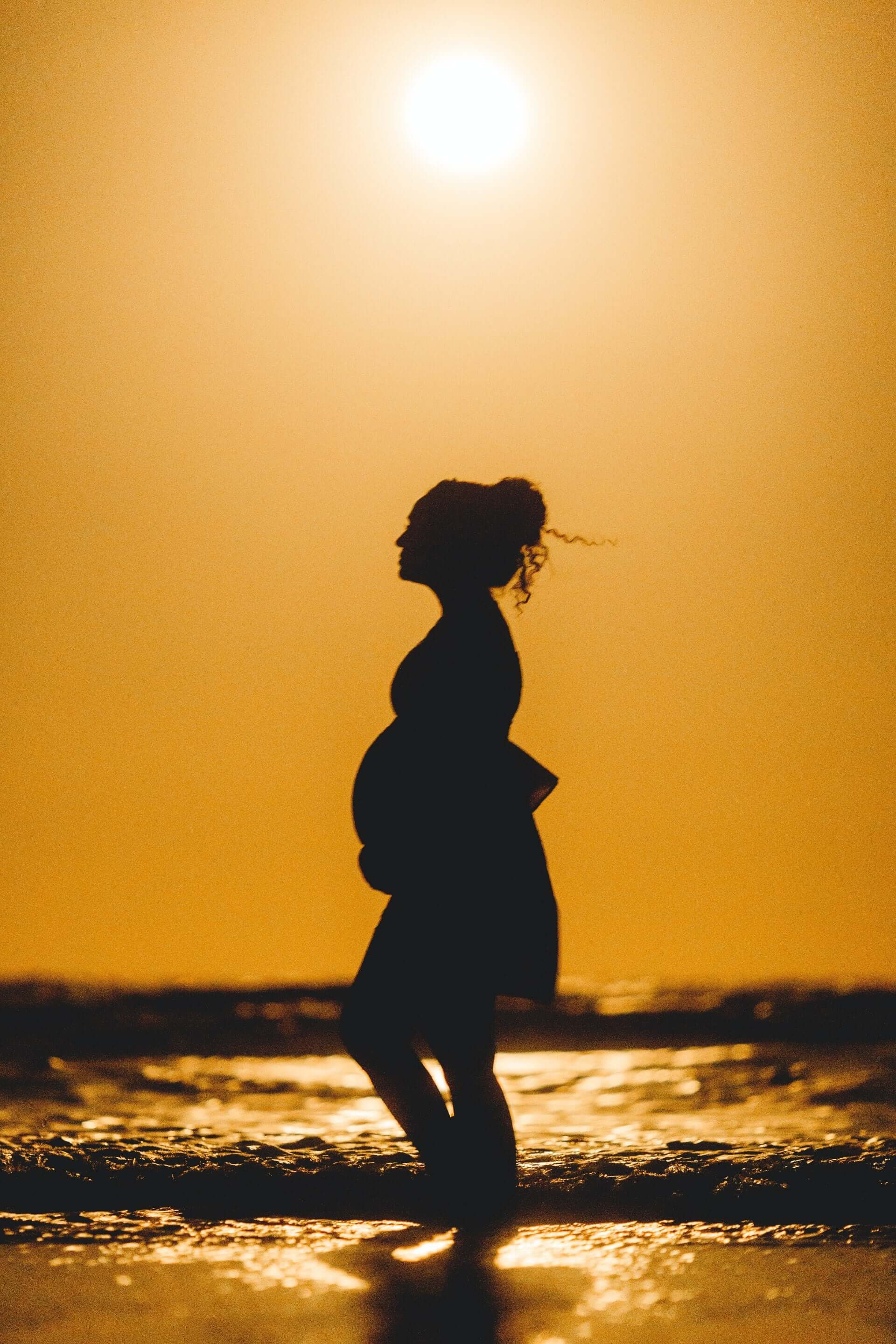 Schwangere Frau läuft beim Sonnenuntergang am Strand entlang