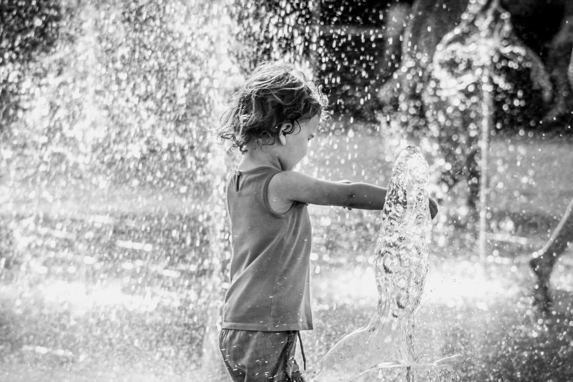 Kind spielt mit Wasserfontänen