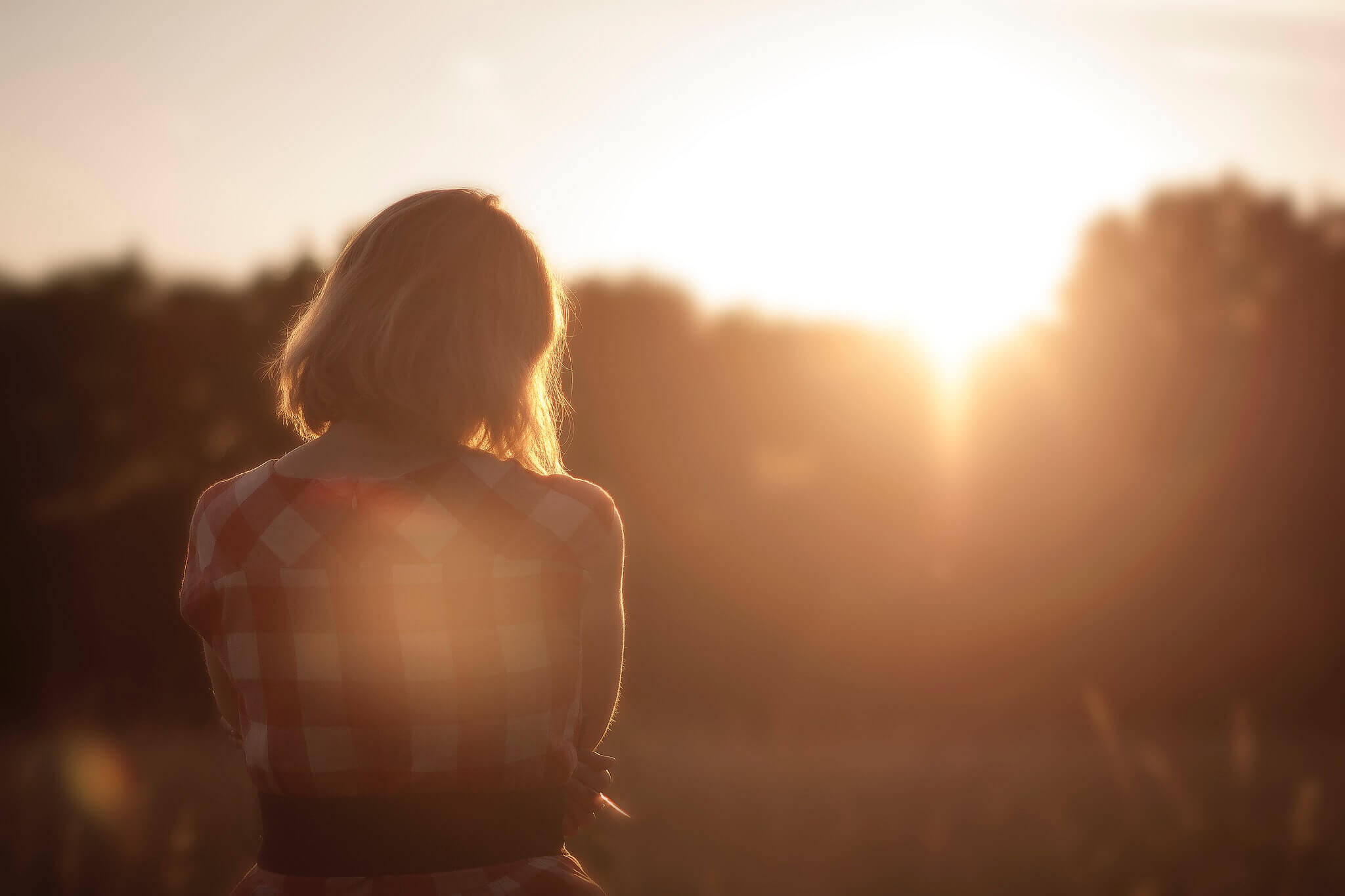 Frau steht mit gebeugtem Kopf im Sonnenuntergang