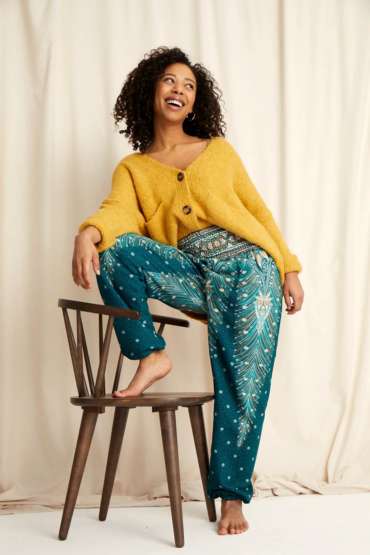 Lachende Frau in warmer Loungewear Haremshose in gemusterten Grüntönen kombiniert mit gelber Strickjacke