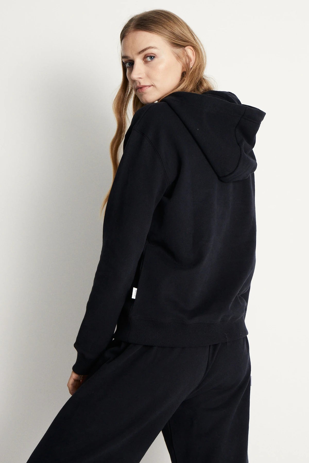 Rückansicht von Frau in warmer Loungewear Haremshose Schwarz kombiniert mit schwarzem Hoodie