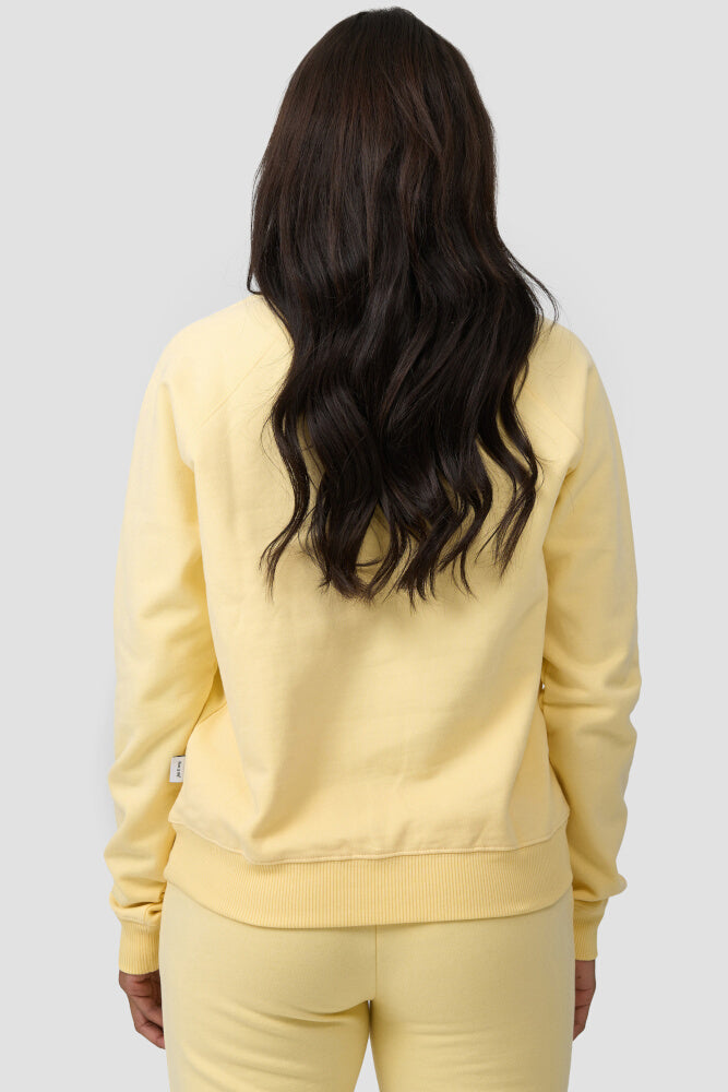 Rückansicht der Frau, die den gelbfarbigen Sweater mit einer gleichfarbigen Sweatpants kombiniert